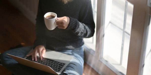 woman in black blouse using laptop and drinking tea