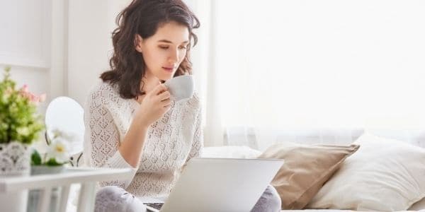 woman in white drinking tea while using laptop